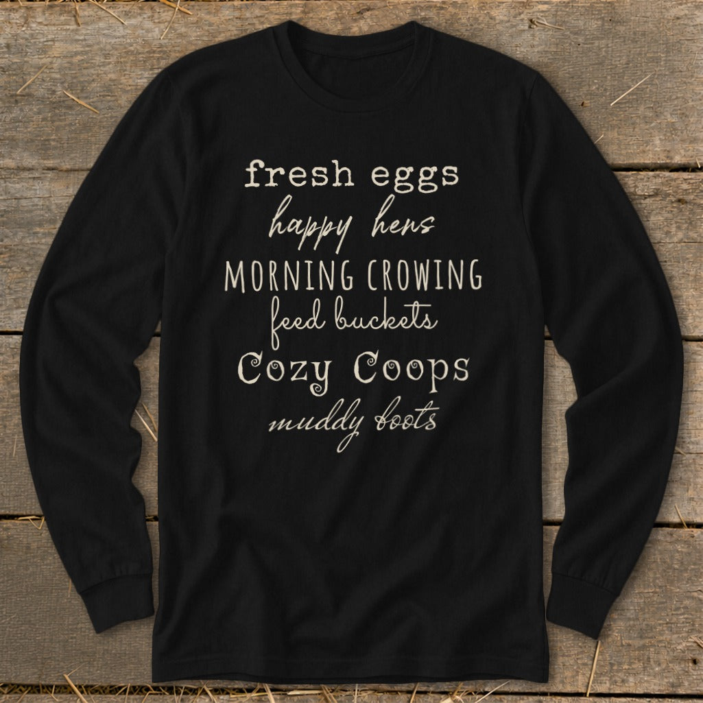 Black long-sleeve shirt with white text: fresh eggs, happy hens, morning crowing, feed buckets, cozy coops, muddy boots.