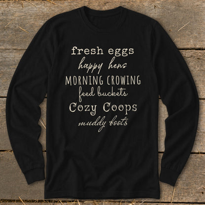 Black long-sleeve shirt with white text: fresh eggs, happy hens, morning crowing, feed buckets, cozy coops, muddy boots.