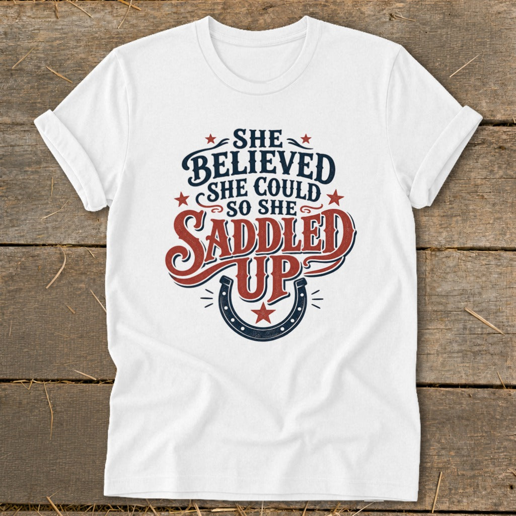 White t-shirt with "She Believed She Could So She Saddled Up" text and horseshoe graphic.