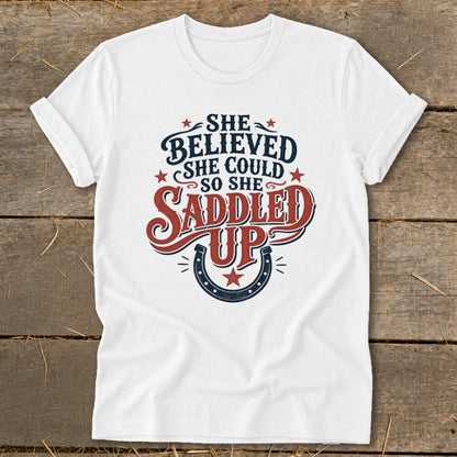 White t-shirt with "She Believed She Could So She Saddled Up" text and horseshoe graphic.
