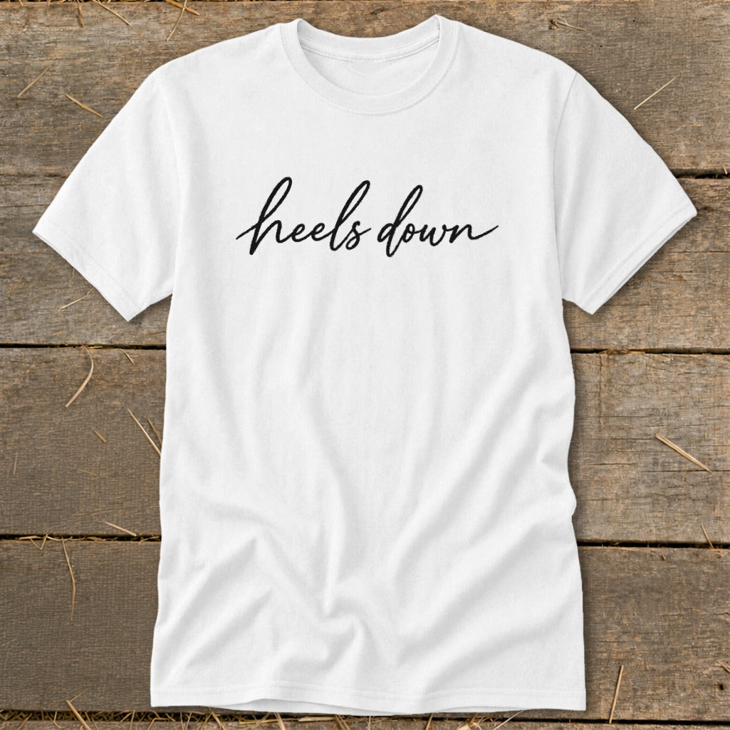 White t-shirt with "heels down" text in black script font.