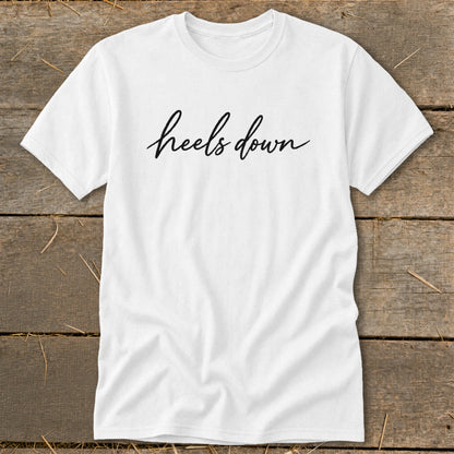 White t-shirt with "heels down" text in black script font.