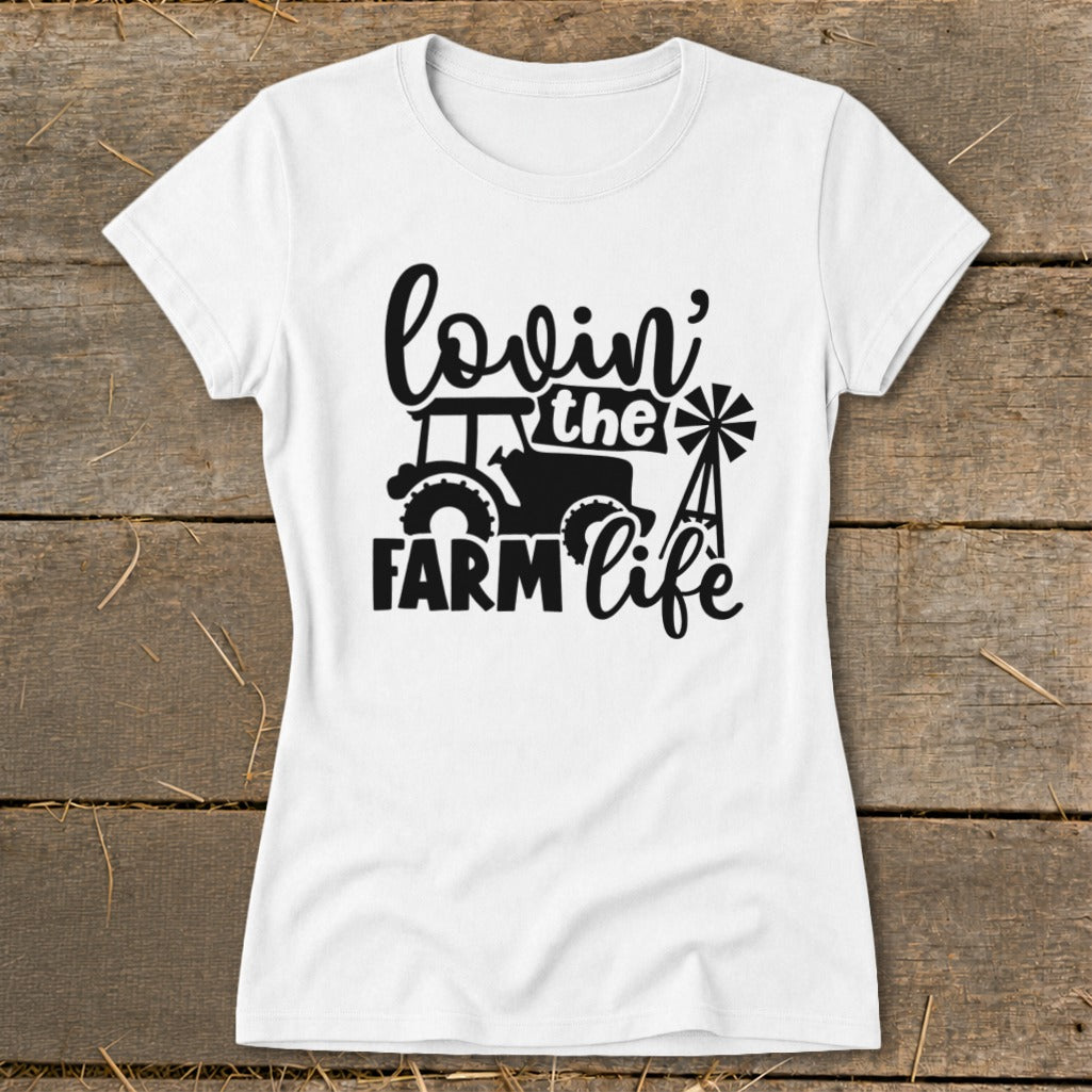 White t-shirt with black text and graphics of a tractor and windmill saying "lovin' the FARM life".