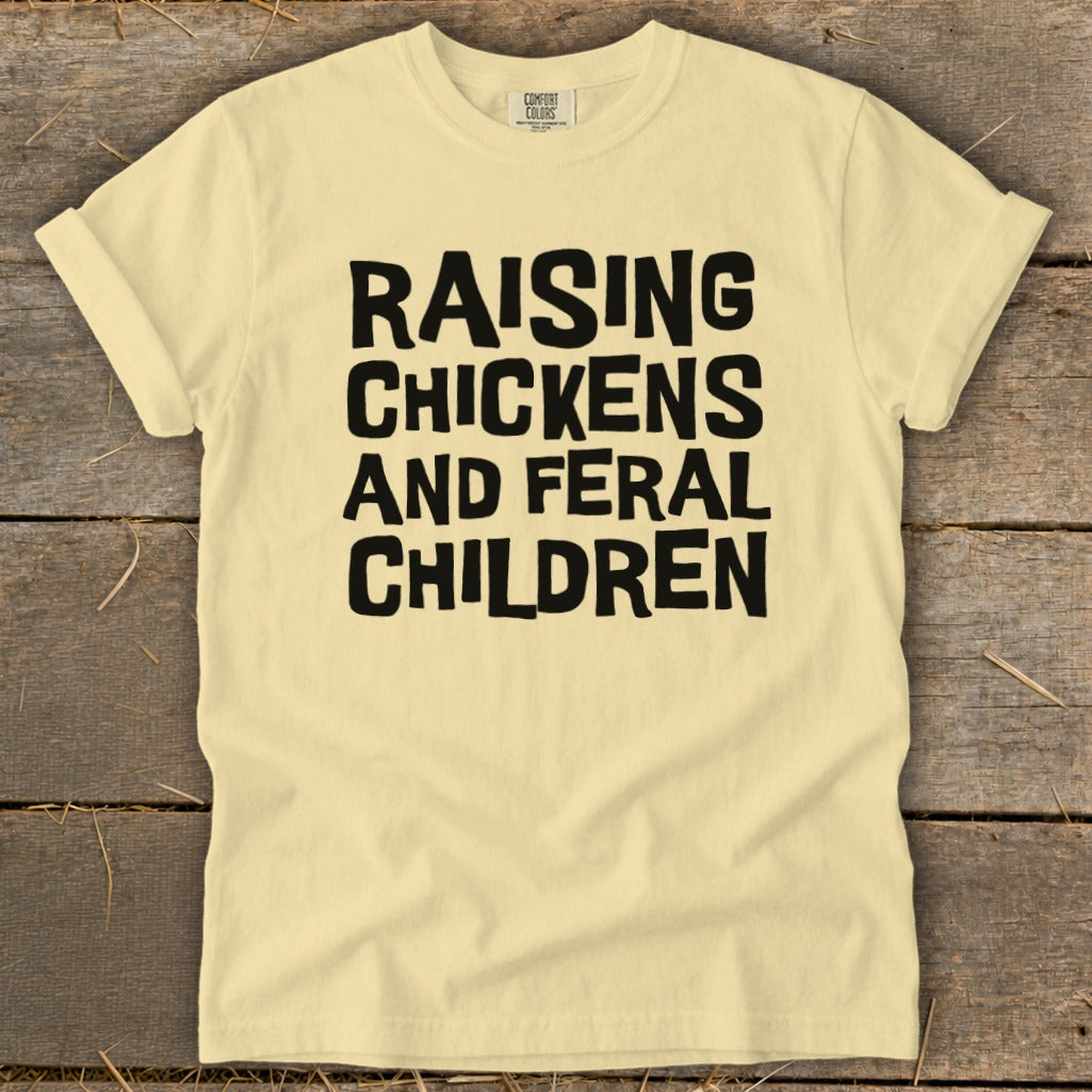 Light yellow t-shirt with black text reading "Raising Chickens and Feral Children".