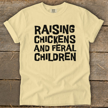 Light yellow t-shirt with black text reading "Raising Chickens and Feral Children".