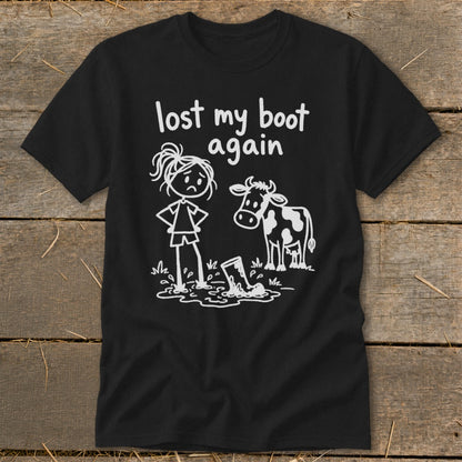 Black t-shirt featuring white text that reads lost my boot again and a cartoon of a girl and cow looking at a muddy boot.
