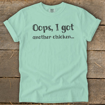 Light green Comfort Colors t-shirt with black text reading "Oops, I got another chicken..."