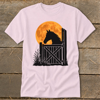 Light pink t-shirt featuring a graphic of a horse silhouette looking over a stable door against a large orange moon.