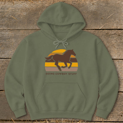 Olive green hoodie with a running horse and sunset graphic and "DOING COWBOY STUFF" text.
