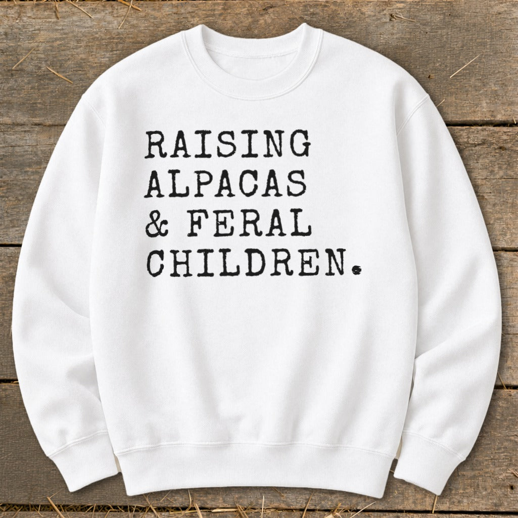 White sweatshirt with black text "RAISING ALPACAS & FERAL CHILDREN."