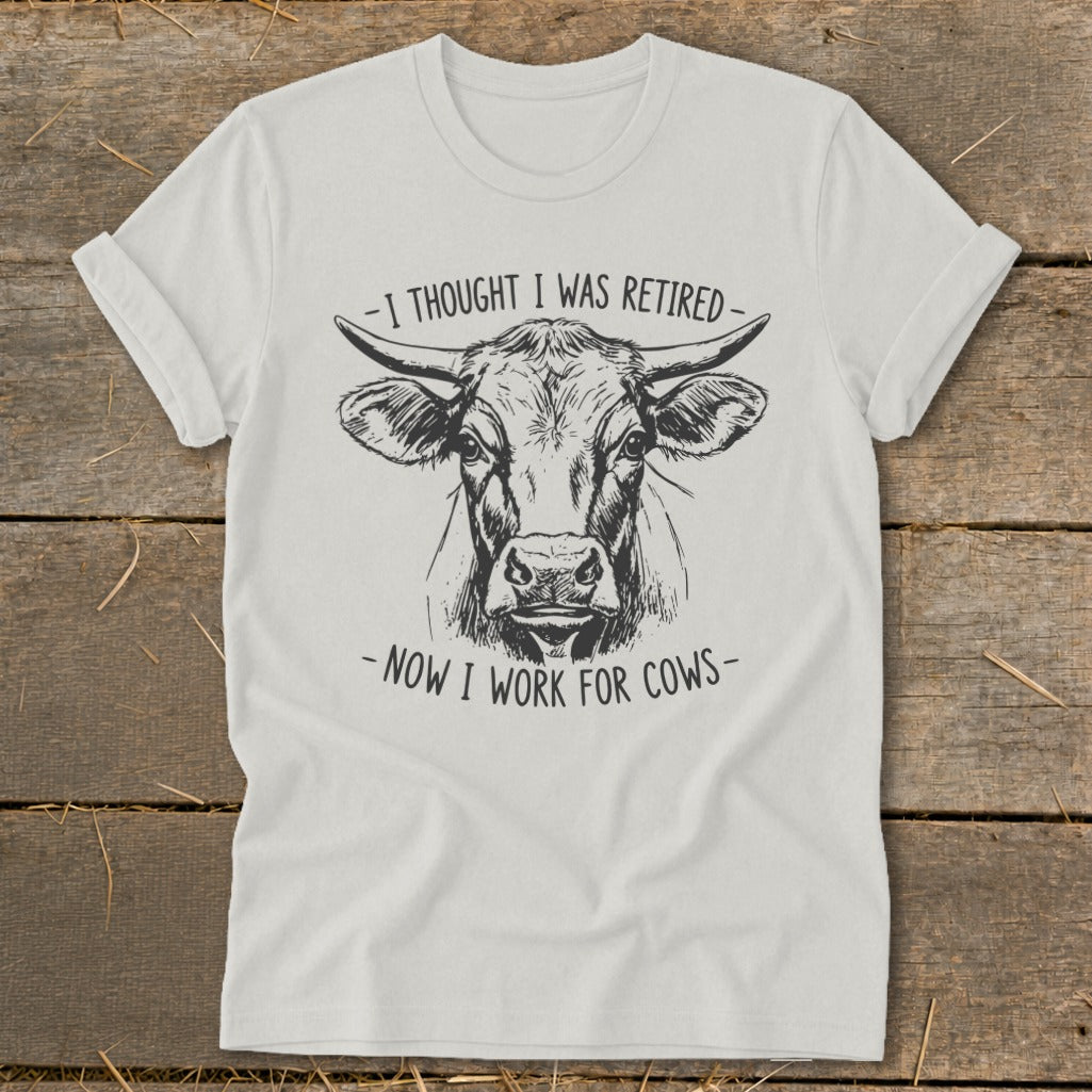 White t-shirt with a cow drawing and text "-I THOUGHT I WAS RETIRED- -NOW I WORK FOR COWS-".
