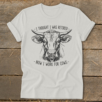 White t-shirt with a cow drawing and text "-I THOUGHT I WAS RETIRED- -NOW I WORK FOR COWS-".
