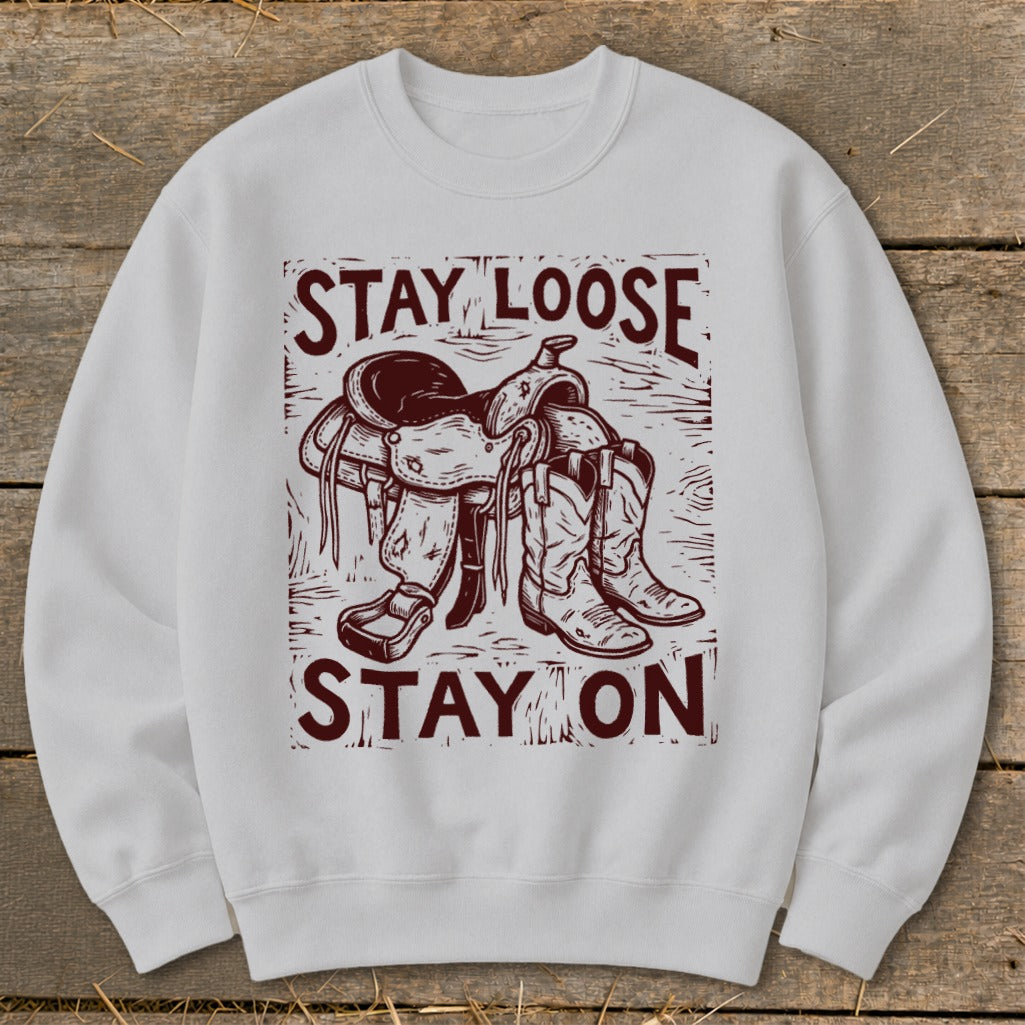 White sweatshirt with maroon graphic of a saddle and boots, reads "STAY LOOSE STAY ON".