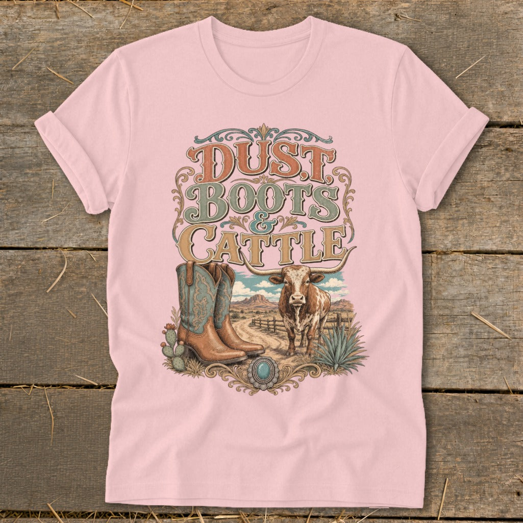 Pink t-shirt print with "Dust Boots & Cattle" text, boots, cow, and desert landscape.