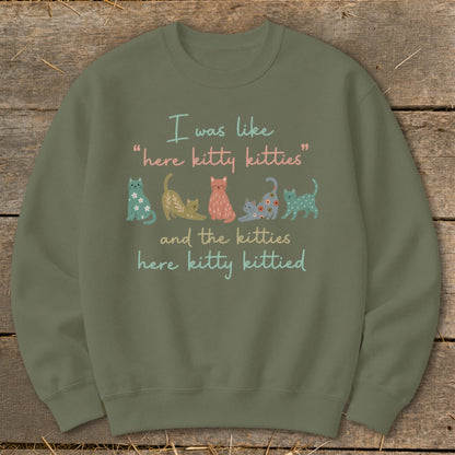 Green sweatshirt with text "I was like 'here kitty kitties' and the kitties here kitty kittied" and cat illustrations.
