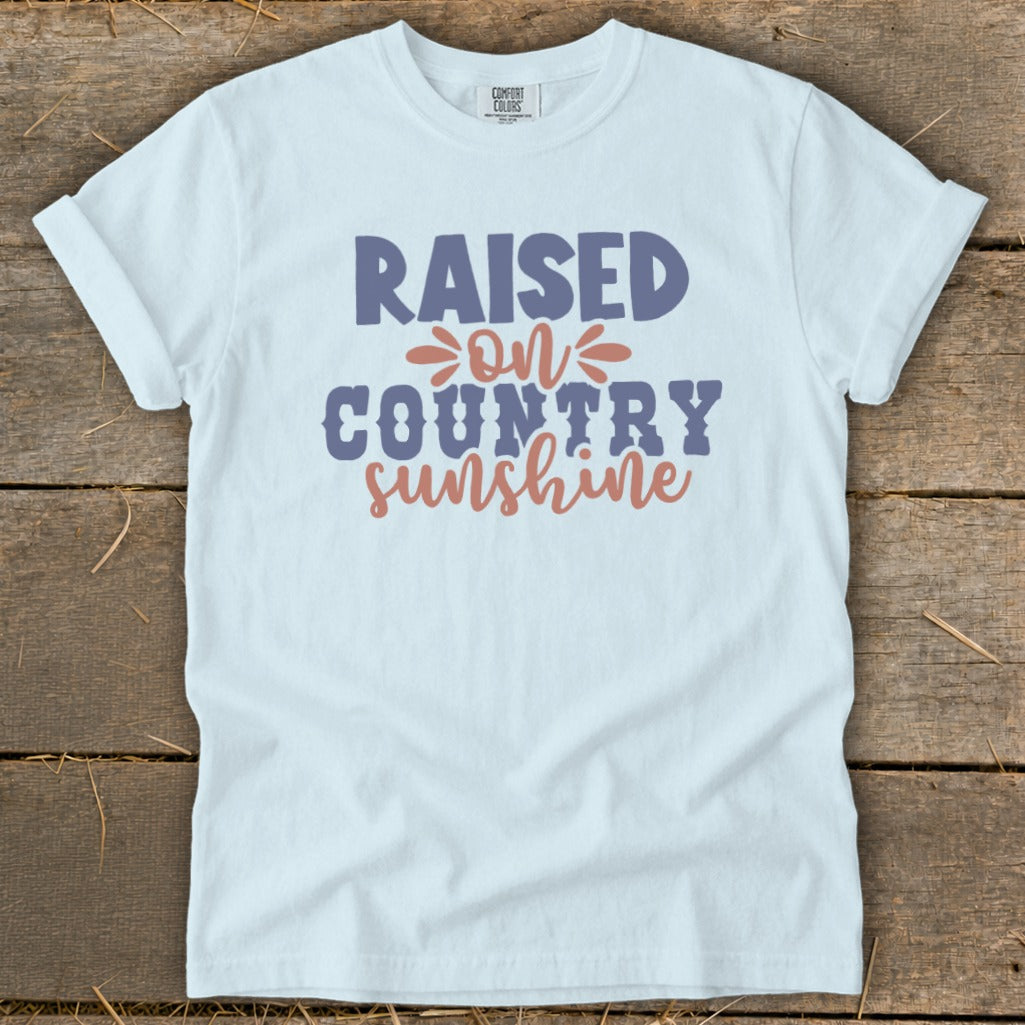 White t-shirt with text "RAISED ON COUNTRY sunshine" in purple and coral.