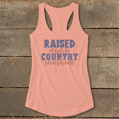 Peach tank top with "Raised on Country Sunshine" text in blue and pink.