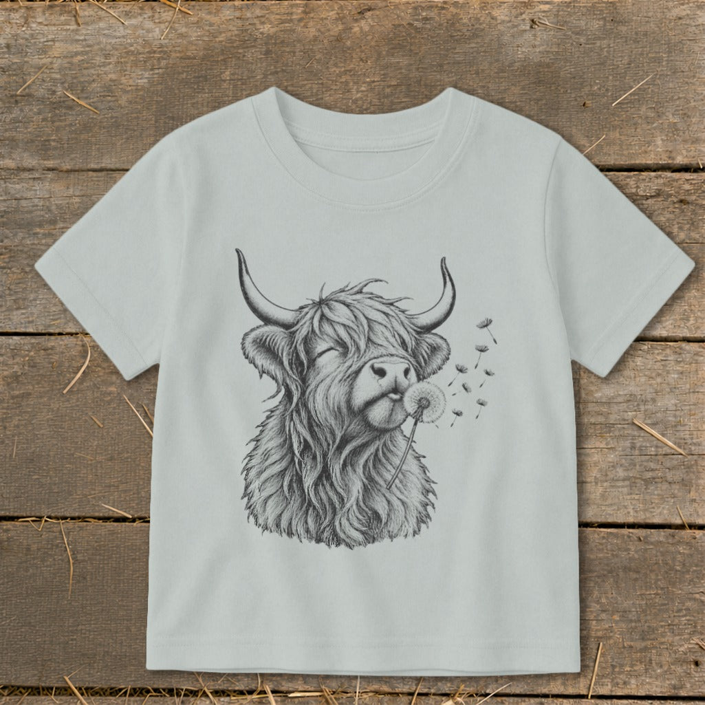 Pencil sketch of a Highland cow blowing a dandelion on a light gray t-shirt.