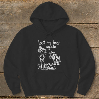 A black hoodie with a white graphic showing a girl standing in mud next to a cow, accompanied by the text lost my boot again.