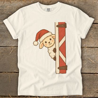 Cream t-shirt with a cartoon sheep wearing a Santa hat peeking from behind a red barn door.