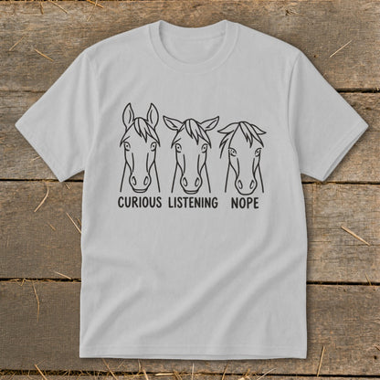A light gray crewneck t-shirt featuring three horse head sketches with the captions curious, listening, and nope.