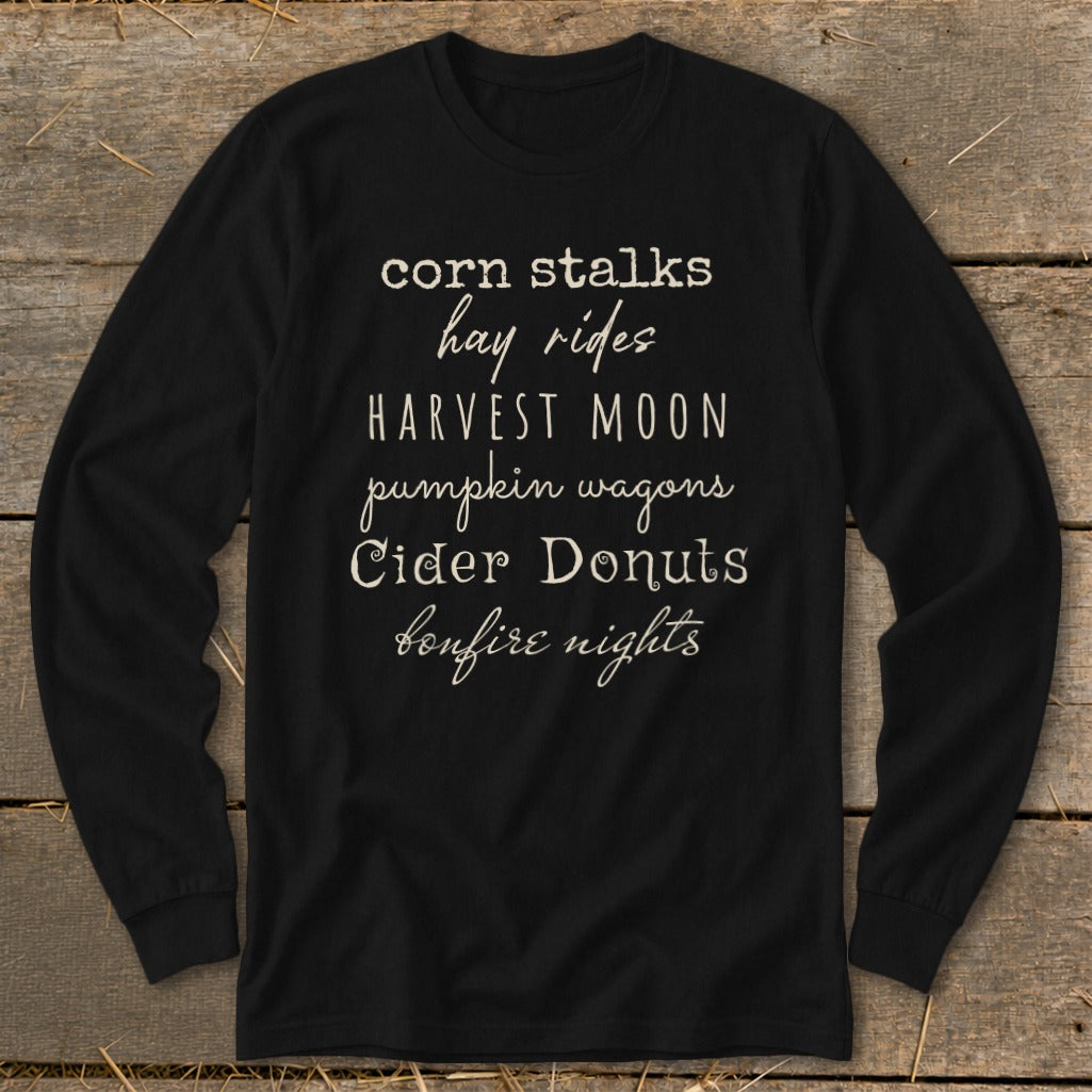 Black long-sleeve shirt with fall phrases: "corn stalks, hay rides, harvest moon, pumpkin wagons, cider donuts, bonfire nights".