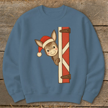 Cute donkey wearing a Santa hat peeking from behind a red barn door.