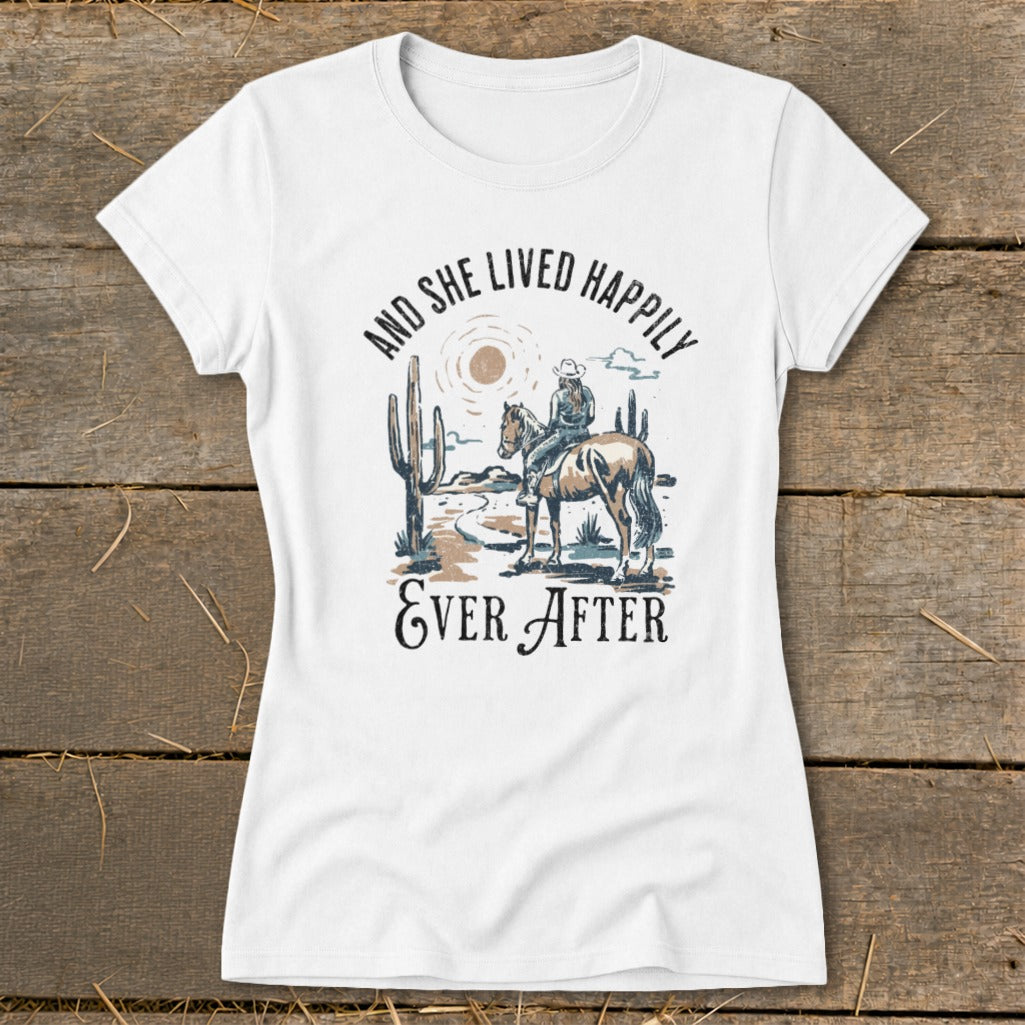 White t-shirt with desert scene graphic: woman on horse, cacti, and text "AND SHE LIVED HAPPILY EVER AFTER".