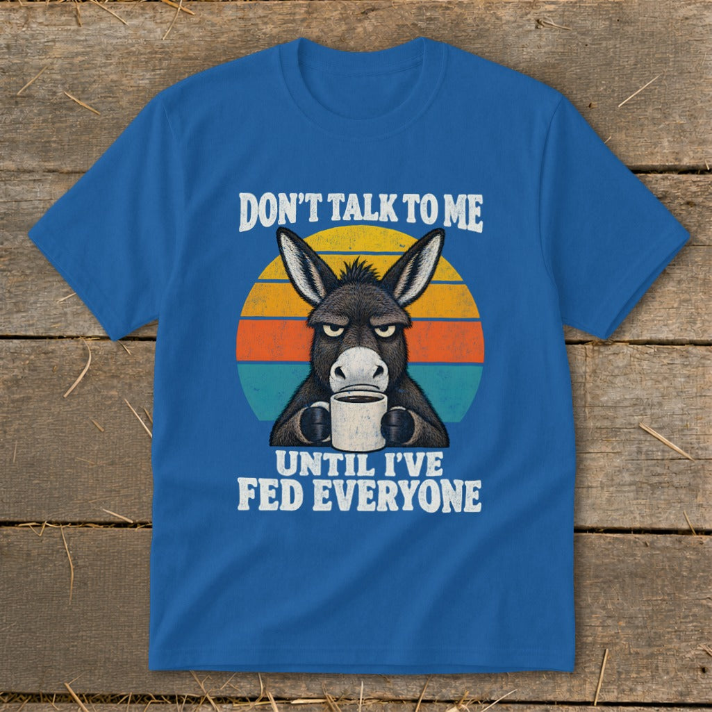 A blue t-shirt featuring a graphic of a grumpy donkey drinking coffee and text reading Don't Talk to Me Until I've Fed Everyone.