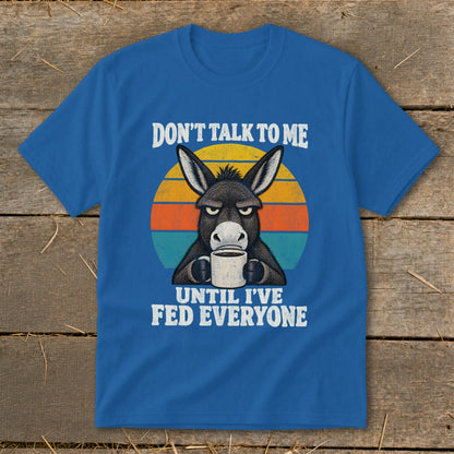 A blue t-shirt featuring a graphic of a grumpy donkey drinking coffee and text reading Don't Talk to Me Until I've Fed Everyone.