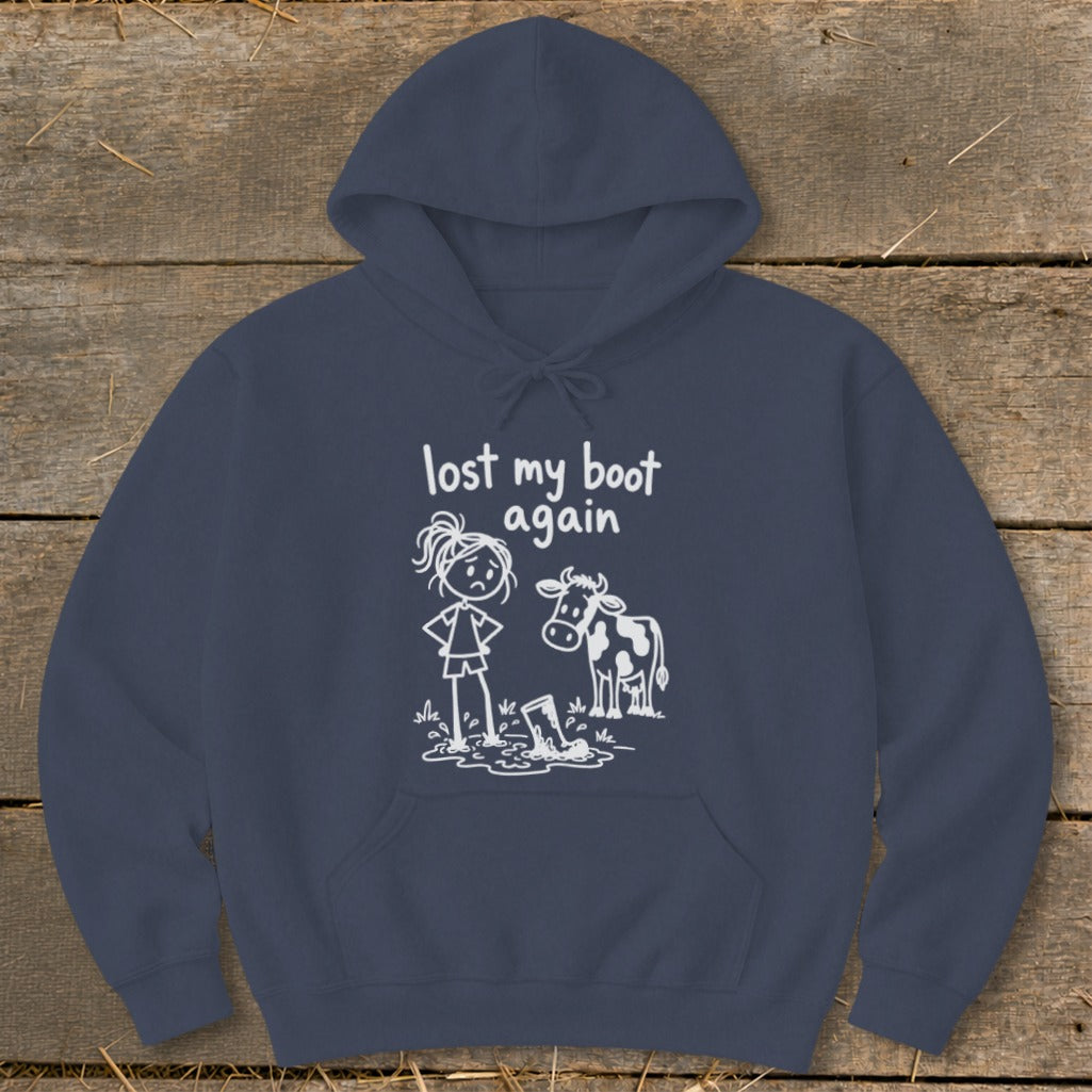 A navy blue hooded sweatshirt features a white graphic of a sad girl and a cow standing near a boot in a muddy puddle, accompanied by the text "lost my boot again."