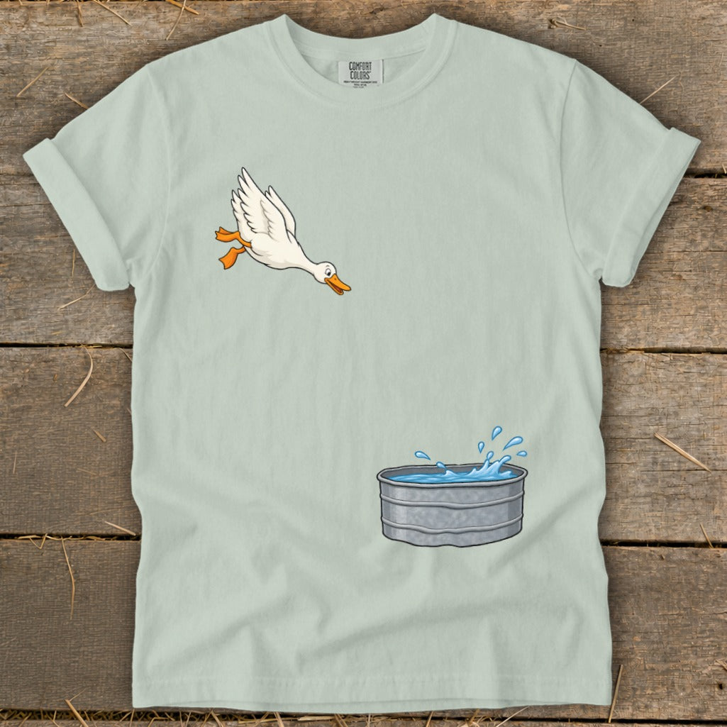 Cartoon duck leaps into a splashing galvanized tub on a light green t-shirt.