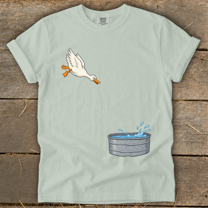 Cartoon duck leaps into a splashing galvanized tub on a light green t-shirt.