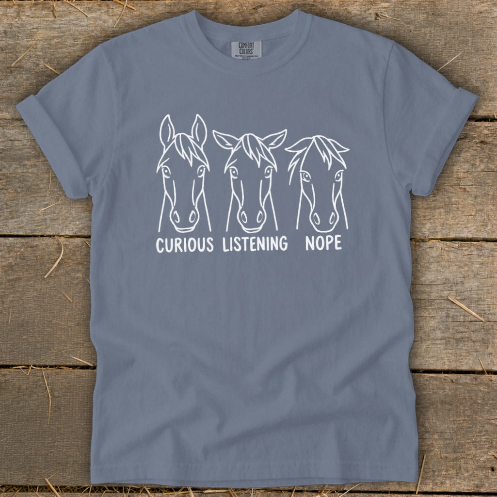 A grey short-sleeved t-shirt with three horse head line drawings and text reading CURIOUS, LISTENING, NOPE.