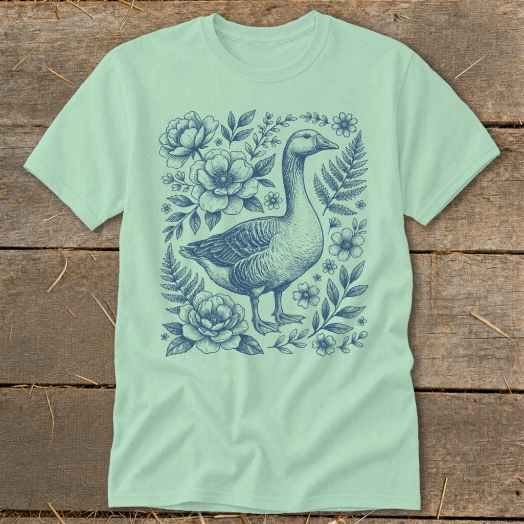 Light green t-shirt with a blue line drawing of a goose surrounded by flowers and ferns.