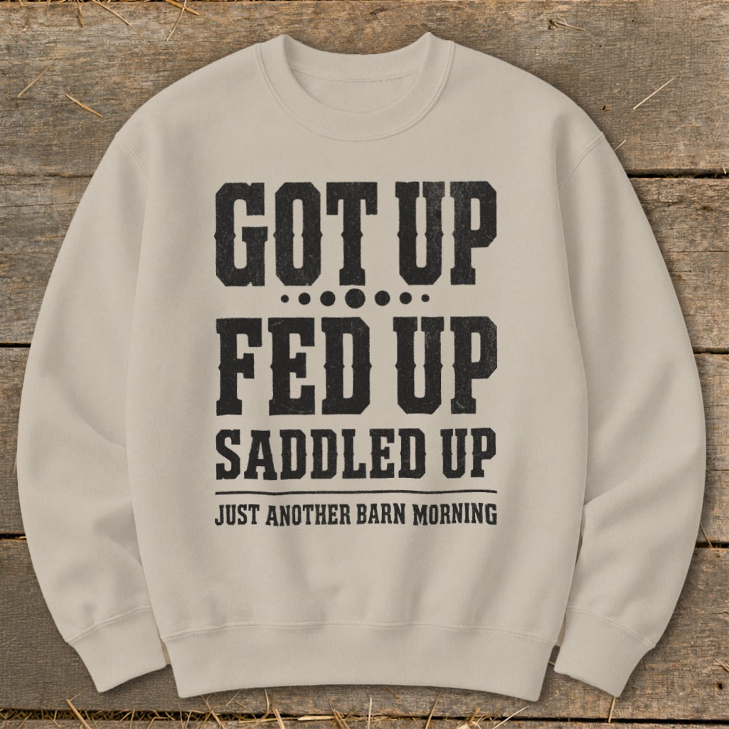 Tan crewneck sweatshirt with distressed black text reading "GOT UP FED UP SADDLED UP JUST ANOTHER BARN MORNING".