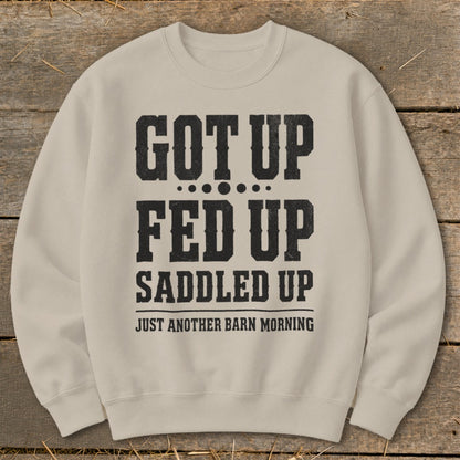 Tan crewneck sweatshirt with distressed black text reading "GOT UP FED UP SADDLED UP JUST ANOTHER BARN MORNING".