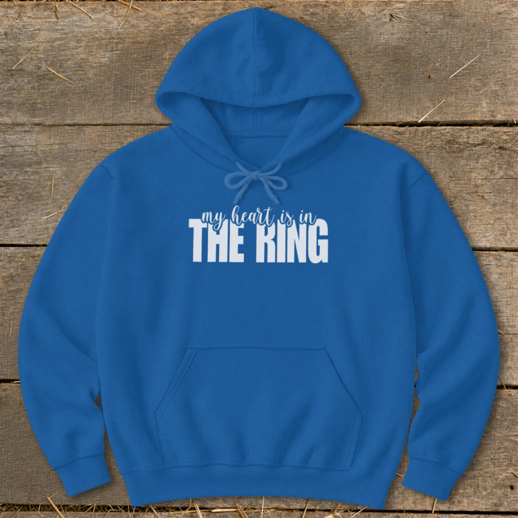 A blue hooded sweatshirt with white text reading my heart is in the ring displayed against a wooden background.