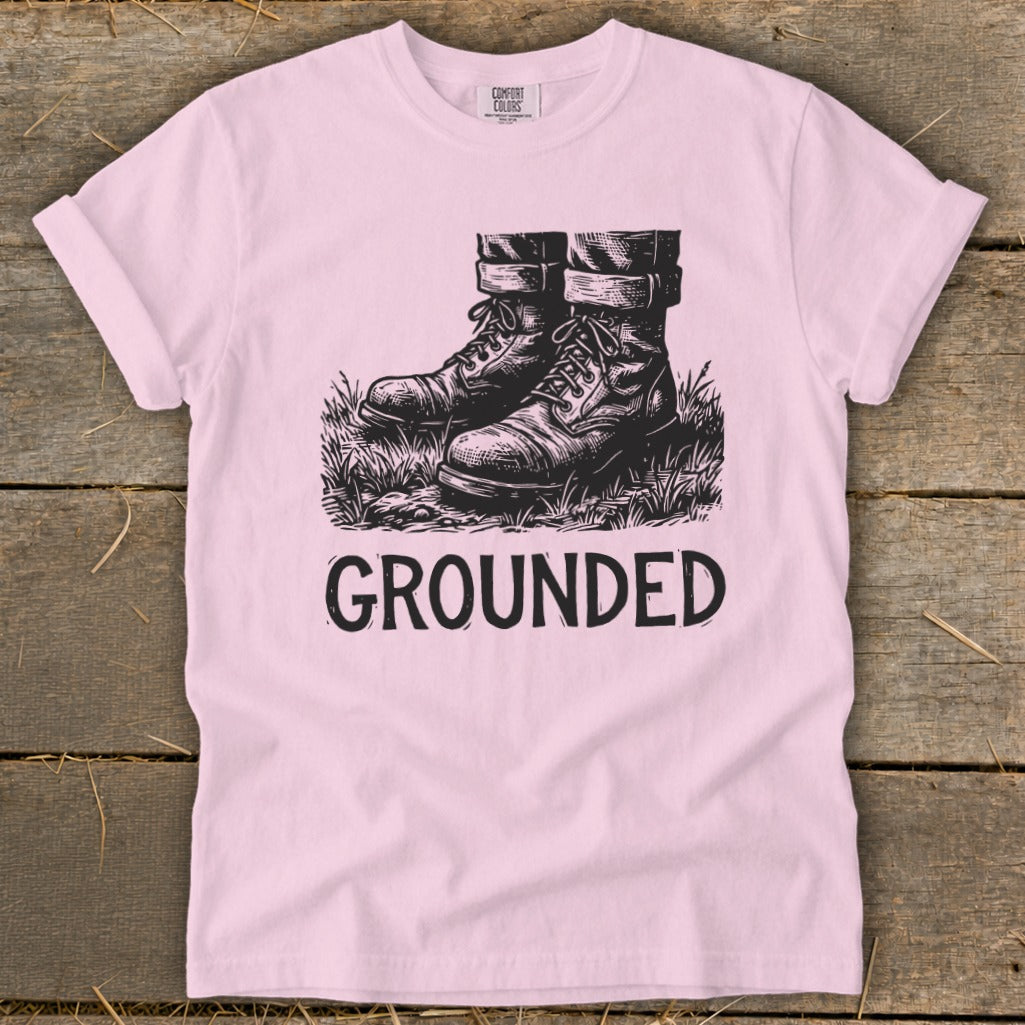 Pink t-shirt with black graphic of boots in grass and the word "GROUNDED".