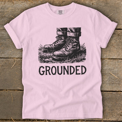 Pink t-shirt with black graphic of boots in grass and the word "GROUNDED".