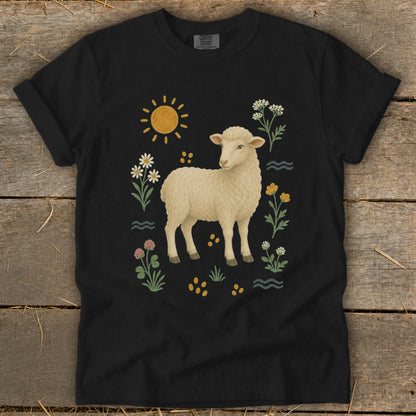 Black t-shirt with a watercolor illustration of a lamb surrounded by flowers, sun, and water.