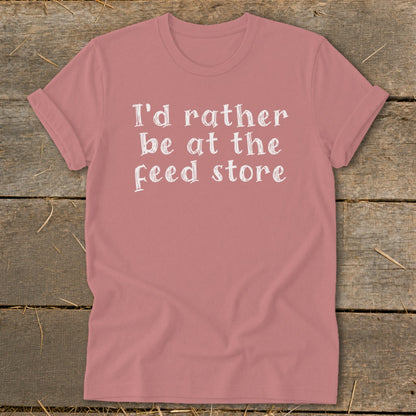 Pink t-shirt with white text that reads "I'd rather be at the feed store."
