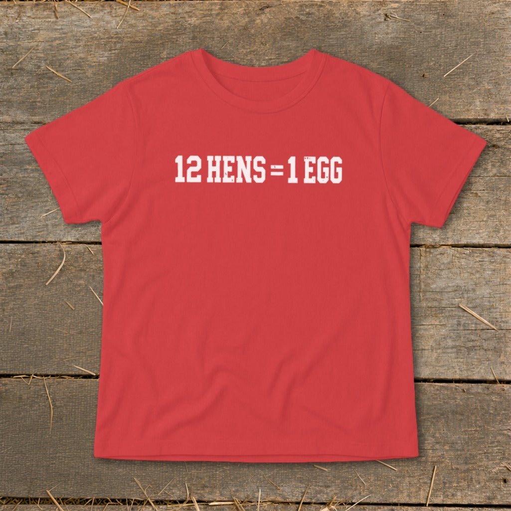 Red t-shirt featuring the white distressed text 12 HENS = 1 EGG, laid flat on a rustic wooden background.