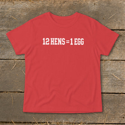Red t-shirt featuring the white distressed text 12 HENS = 1 EGG, laid flat on a rustic wooden background.