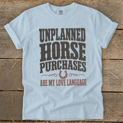 Light blue t-shirt with "Unplanned Horse Purchases Are My Love Language" text and horseshoe graphic.