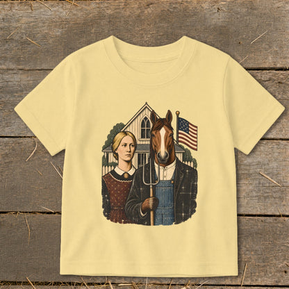 A light yellow short-sleeved t-shirt featuring an illustration of an American Gothic style couple with a horse head holding a pitchfork.