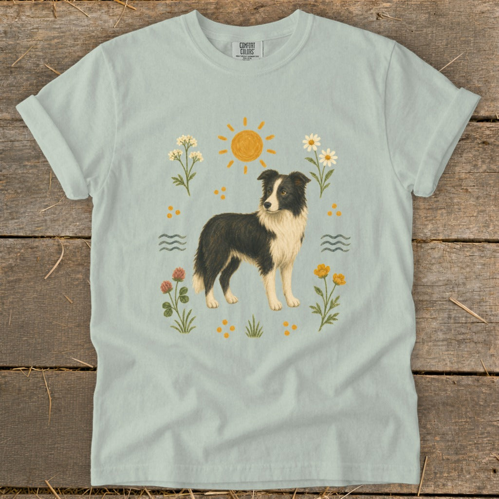 Light blue t-shirt with a border collie illustration surrounded by flowers, sun, and water.