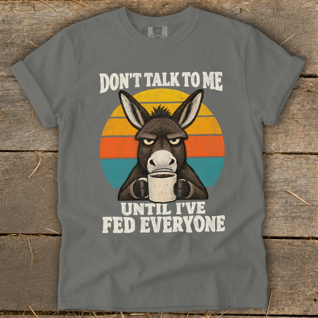 A grey t-shirt featuring a grumpy donkey holding a coffee mug, with retro sunset stripes and text.