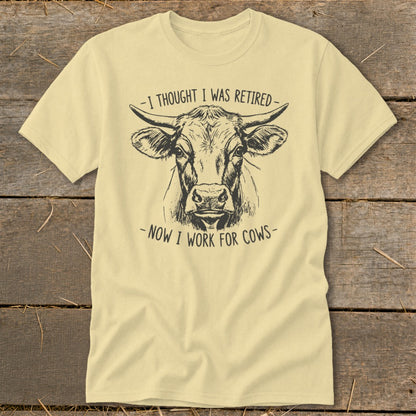 Light yellow t-shirt with a sketch of a cow and text, "I thought I was retired - Now I work for cows."