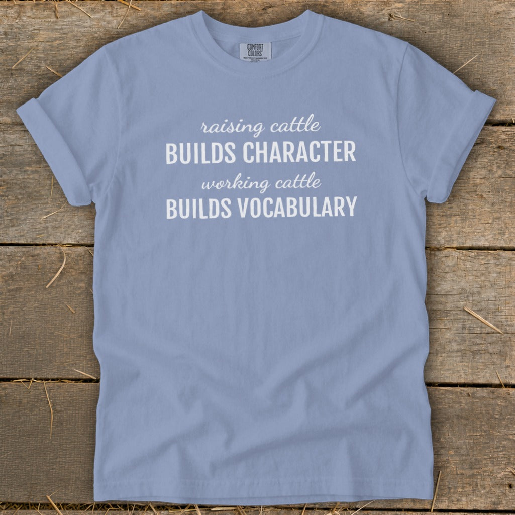 Light blue t-shirt with white text reading "raising cattle BUILDS CHARACTER, working cattle BUILDS VOCABULARY."